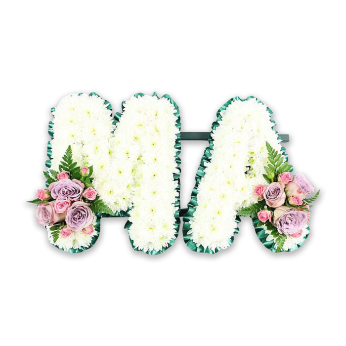 A beautifully balanced funeral letter arrangement spells out MA in bold, upright capitals, clearly photographed against a white background that makes the flowers stand out in quiet clarity. Each letter is thickly covered with white chrysanthemums, their round flower heads placed shoulder to shoulder so no gaps in the base can be seen. The chrysanthemums' fine, feathery petals overlap to create a gently undulating surface, soft and inviting to the touch, like a field of tiny, snowy blooms. Surrounding the outer edges of both letters is a dark emerald-green satin ribbon, arranged in delicate, regular pleats. The ribbon's subtle sheen catches the light, giving a sophisticated frame that accentuates the curves and angles of the M and A, while the deep green creates a classic contrast to the bright white flowers. A slender dark green bar along the bottom discreetly joins the two letters, helping them sit as a single, unified tribute. At the base of the left leg of the M and the right leg of the A, matching floral sprays introduce gentle colour. These clusters feature soft pink roses, muted lilac roses, and small pink spray roses nestled closely together, their velvety petals opening into layered spirals. Airy fern fronds and a touch of leafy greenery emerge from behind the roses, lending a natural, garden-inspired flourish that softens the overall look. The tribute feels deeply personal, as though chosen for a much-loved mum in Cobham, perhaps for a service at a local church off the High Street or near Fairmile. It radiates tenderness and gratitude, offering a graceful way to say thank you and goodbye through delicate flowers and calm, harmonious colour.