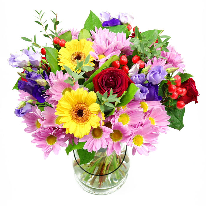 A vibrant, garden-inspired bouquet is captured here in a clear glass vase that reveals every carefully placed stem, all set against a plain white background so the colours appear especially vivid. At the very centre, a gathering of deep red roses opens in plush, velvety spirals, their saturated tone and classical form giving the whole arrangement a tender, romantic core. Beside them, bright yellow gerbera daisies with rich brown-orange centres act as cheerful counterpoints, their broad, daisy-shaped blooms evoking the sunny, welcoming feel of Cobham's village cafés on a bright day. Around this central cluster, a profusion of pink and soft lilac daisies or chrysanthemums spreads outward, each flower composed of many fine petals encircling a delicate yellow eye. These daisy-like blossoms lend the bouquet volume and a soft, comforting texture, as if you could almost sink your hands into them like a cushion of petals. Slender stems of lisianthus in tones of purple and lavender thread gently through the design, their bell-shaped, slightly ruffled flowers providing pockets of cool colour and a sense of graceful movement, reminiscent of wildflowers dancing near the trails by the River Mole. Between the blooms, bright red hypericum berries sit like polished beads, their smooth, rounded forms offering visual contrast and a touch of playful detail. Various shades of green foliage fan outward-broad, glossy dark leaves giving structure and lighter, more delicate sprigs adding lift and freshness. Through the vase, the straight, neatly trimmed stems stand immersed in clear water, underscoring the bouquet's freshness and the attentive eye of a skilled florist. This composition feels both abundant and carefully curated, ideal for same-day delivery to a home near Cobham & Stoke D'Abernon station or as a centerpiece for an intimate gathering in Fairmile, filling the space with colour, texture, and an air of joyful celebration.