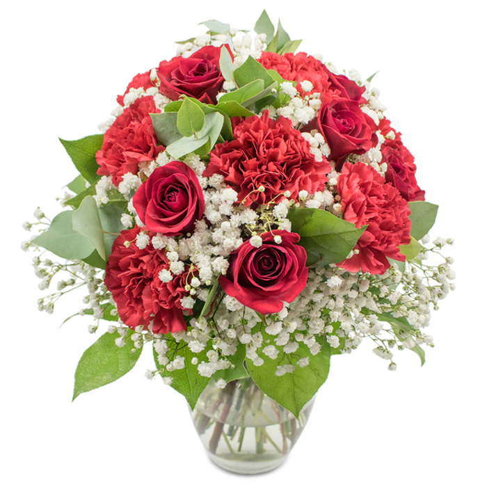 A classic red and white floral arrangement is displayed in a simple clear glass vase, standing out crisply against a clean white studio background that throws every petal and leaf into sharp relief. At the heart of the bouquet are several deep red roses, rich in tone and velvety to the eye, their tightly layered petals spiralling inward with that familiar, timeless shape associated with romance and devotion. Surrounding these are numerous red carnations, each bloom full and frilled, their intricate, ruffled petals overlapping in waves that add generous volume and plush texture to the design. Interwoven among the bold reds is a generous scattering of white baby's breath, its countless tiny blossoms on slender green stems forming a soft, cloud-like halo that lightens the arrangement and introduces a sense of innocence and sincerity. Fresh greenery is tucked throughout: dark green rose leaves and rounded, silvery eucalyptus leaves create depth, contrast, and a hint of the natural beauty you might see on a walk through the green lanes around Cobham's Fairmile or the paths near Painshill Park. The bouquet is constructed into a rounded dome, neat and well balanced, suggesting the careful hands of a Cobham florist who understands both proportion and emotion. The stems inside the vase are clearly visible in the water, aligned and freshly cut, speaking to early-morning preparation and readiness for delivery to homes and businesses from Cobham High Street to Downside. Bright, even lighting emphasises the vivid reds, crisp whites, and fresh greens, conveying a feeling of celebration and intimate warmth ideal for anniversaries, Valentine's Day dinners, or heartfelt romantic gestures in Cobham.